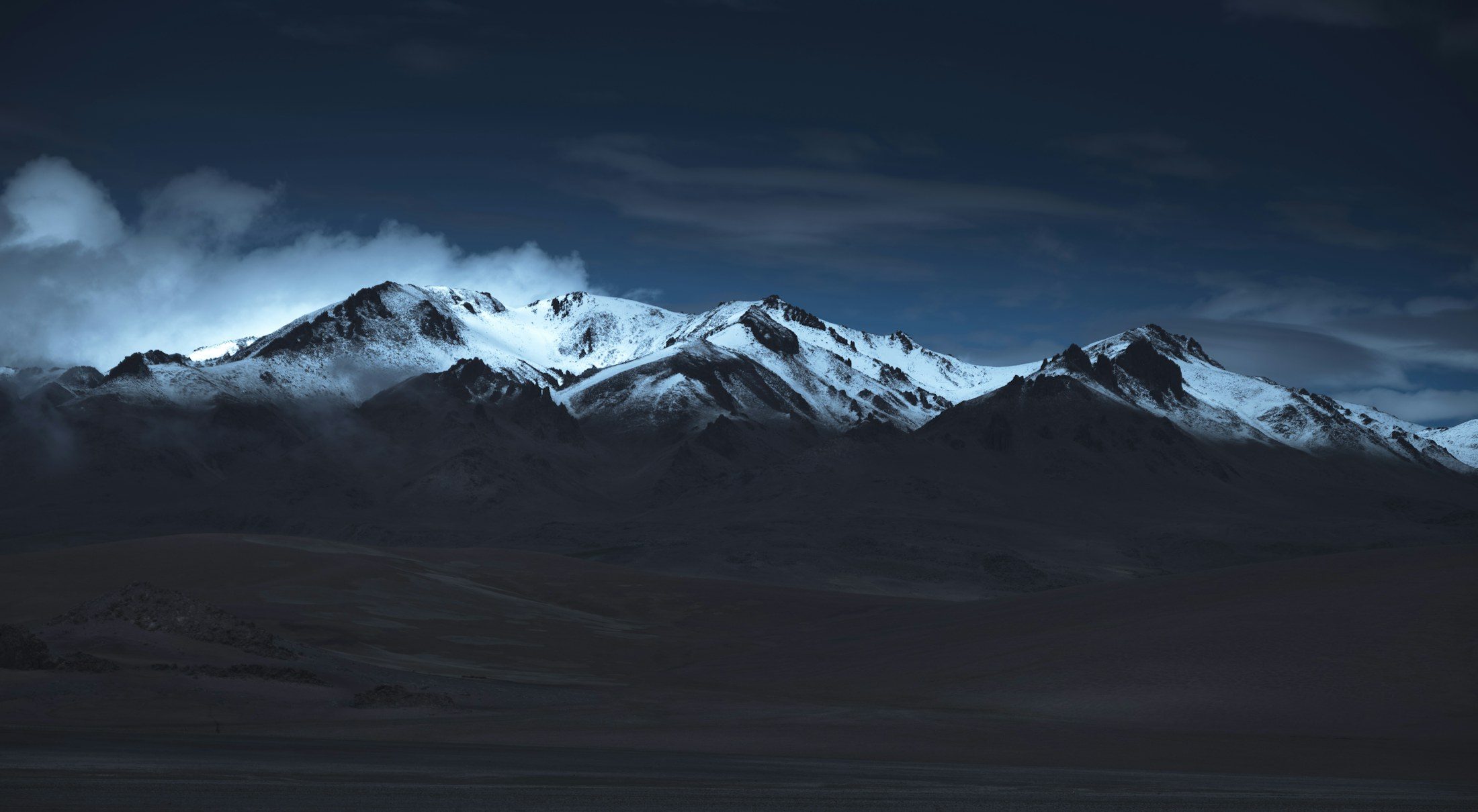 A dark snow-capped mountain range at dusk